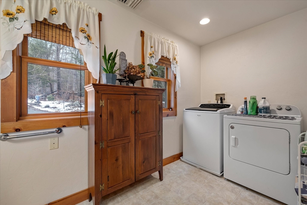 Laundry room with a white washer and dryer beside a wooden cabinet and windows overlooking a snowy yard.