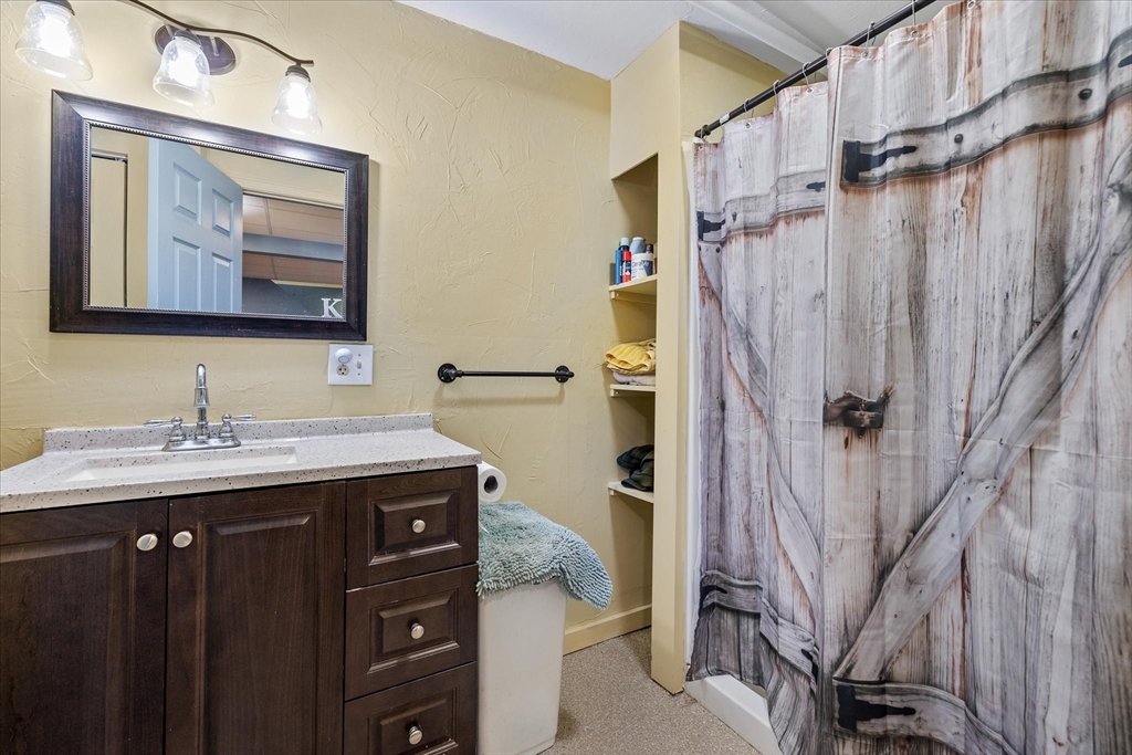 Bathroom with a dark wood vanity, framed mirror, and wood-plank-pattern shower curtain.