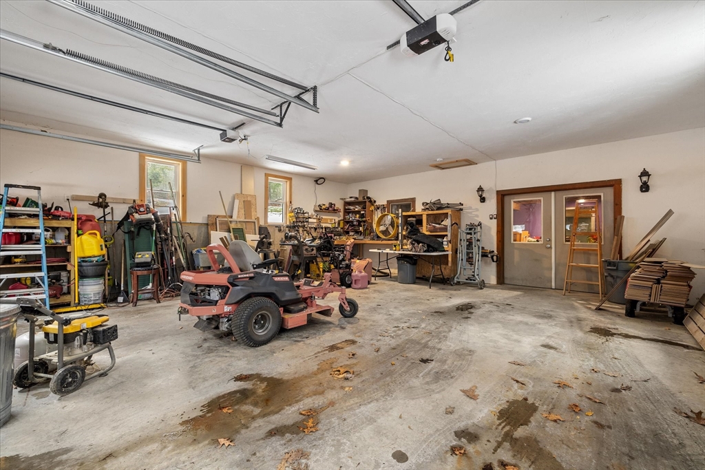 Garage workshop with a red riding mower, crowded workbenches, and tools along the walls.