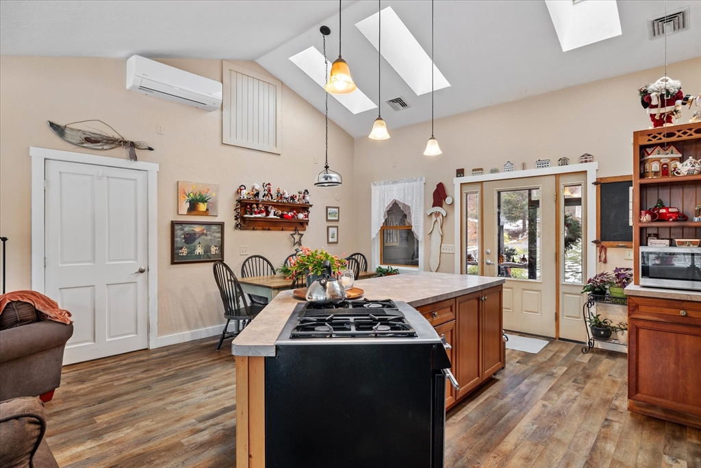 Kitchen with a large island and gas cooktop beneath skylights, with glass doors and a dining area.