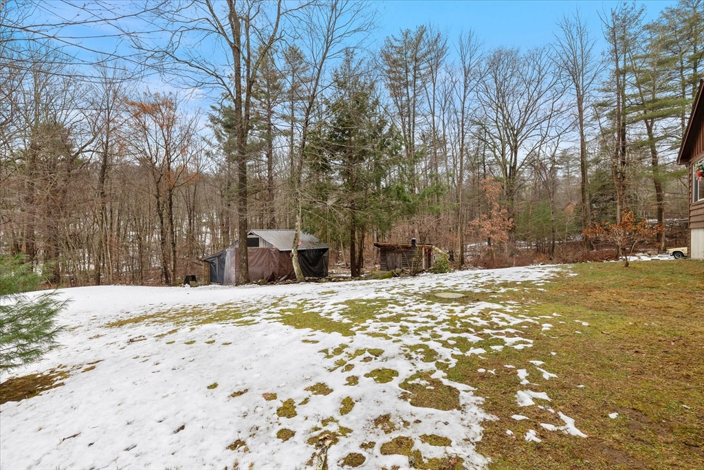 Snow-dappled yard with two outbuildings at the edge of leafless woodland.