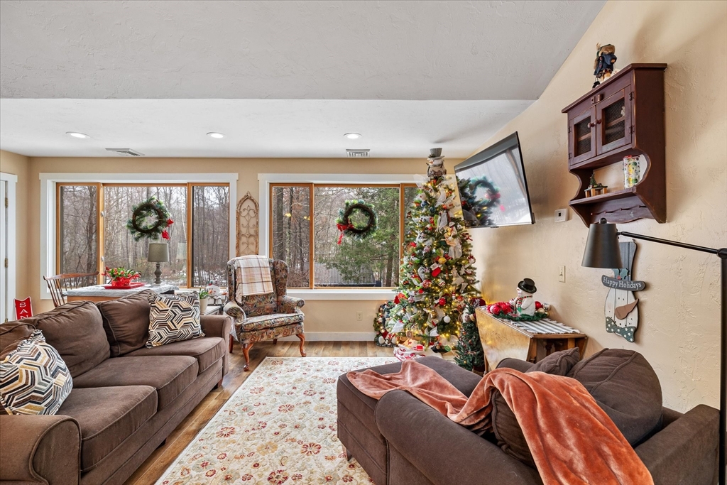 Living room with brown sofas, a decorated Christmas tree, and large windows overlooking leafless woods.