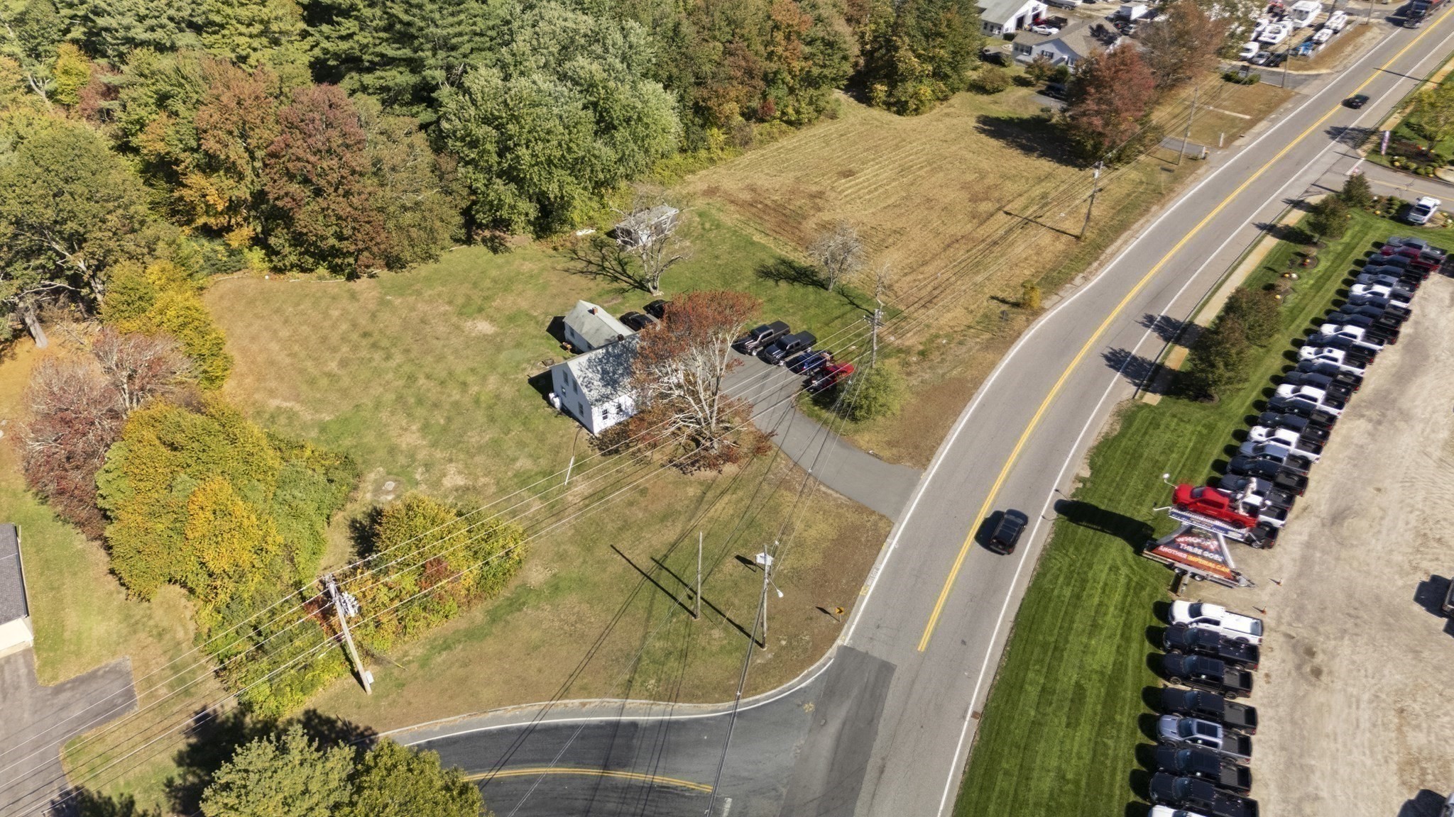 Aerial view of a white house on a spacious, tree-lined lot beside a paved road.