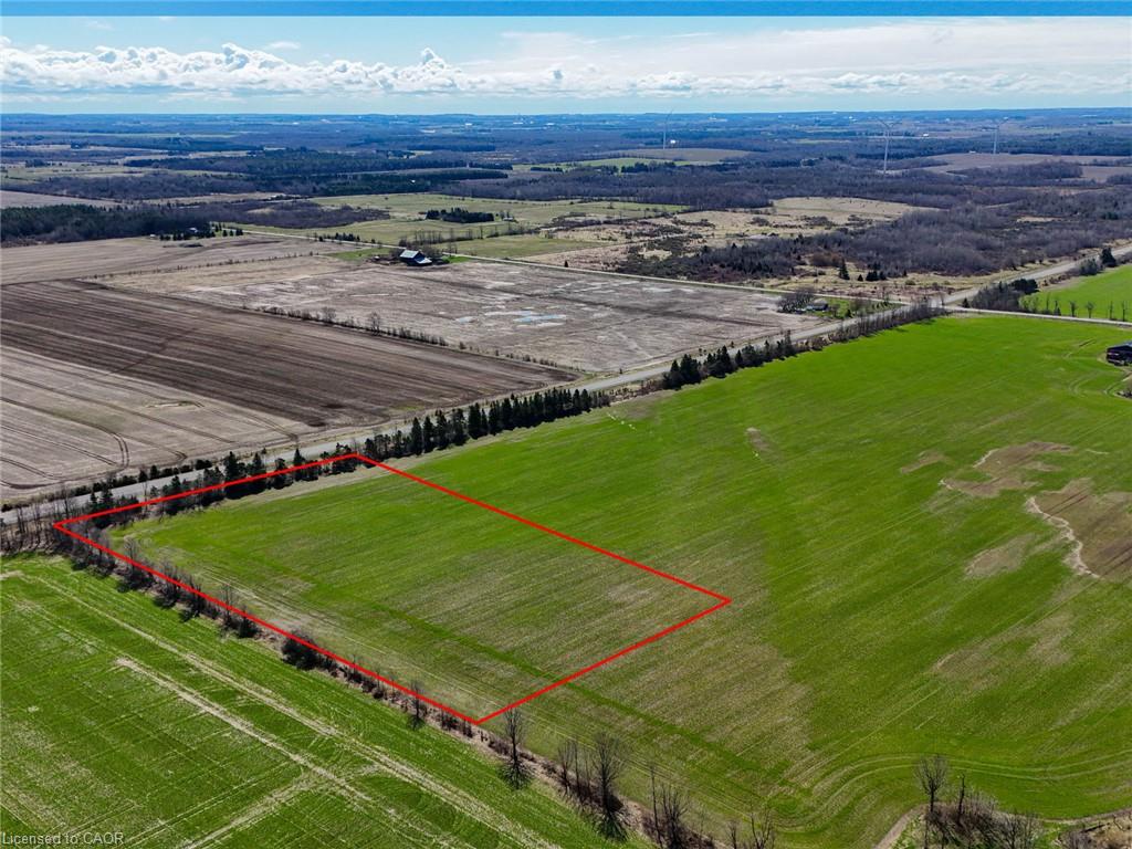 Aerial view of a green rural field outlined in red, with tree-lined edges and surrounding farmland.