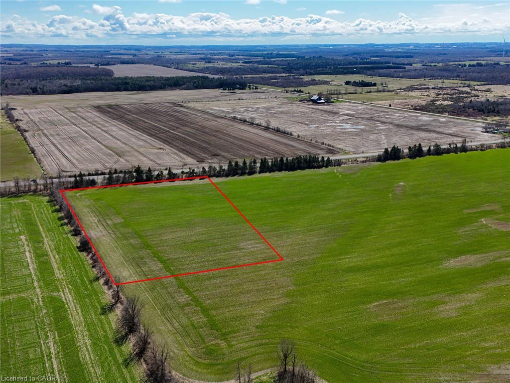 Aerial view of a green parcel outlined in red, surrounded by farmland and distant countryside.