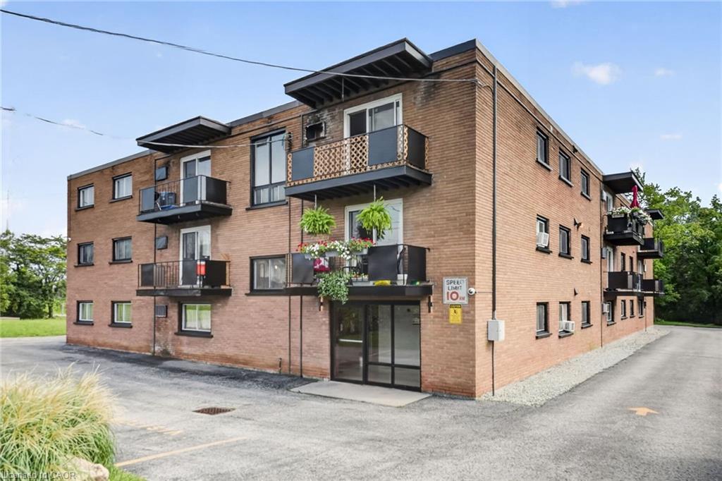 Brick apartment building with balconies and a glass entrance beside its paved parking area.
