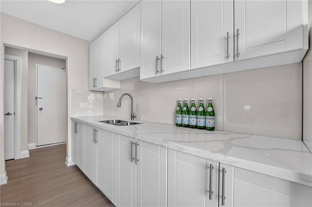 Modern white kitchen with long veined countertops, glossy backsplash, and green bottles on the counter.