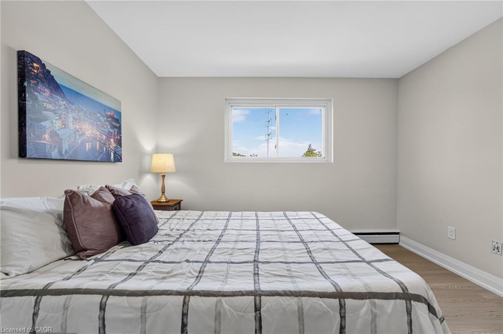 Bedroom with a large plaid-covered bed, mauve pillows, and a framed cityscape print.