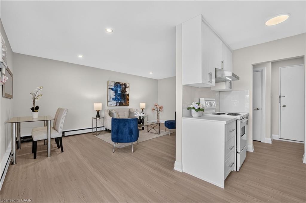 Open-concept condo kitchen and living area with a breakfast bar, blue chairs, and light wood floors.