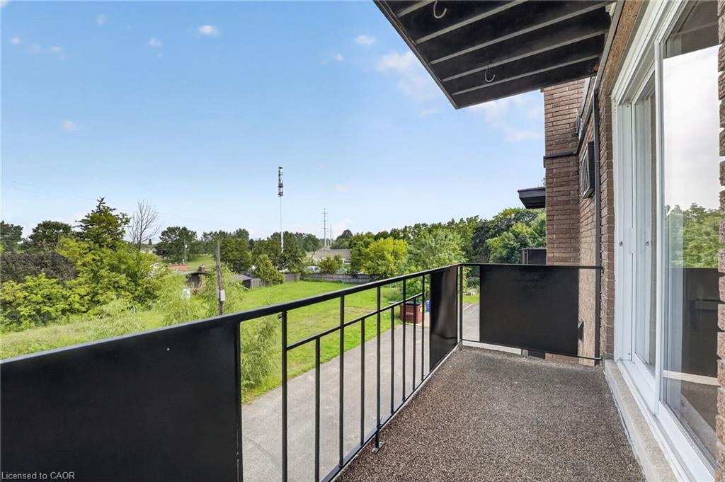 Apartment balcony with black railings overlooking a grassy area and trees.