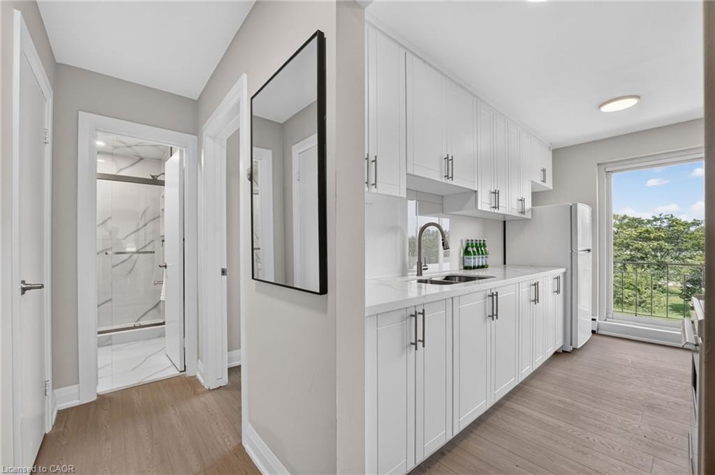 Kitchen with white shaker cabinets, wood-look floors, and a sliding door to a tree-lined balcony.