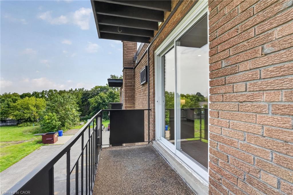 Residential balcony with brick walls, sliding glass doors, and a view of green trees.