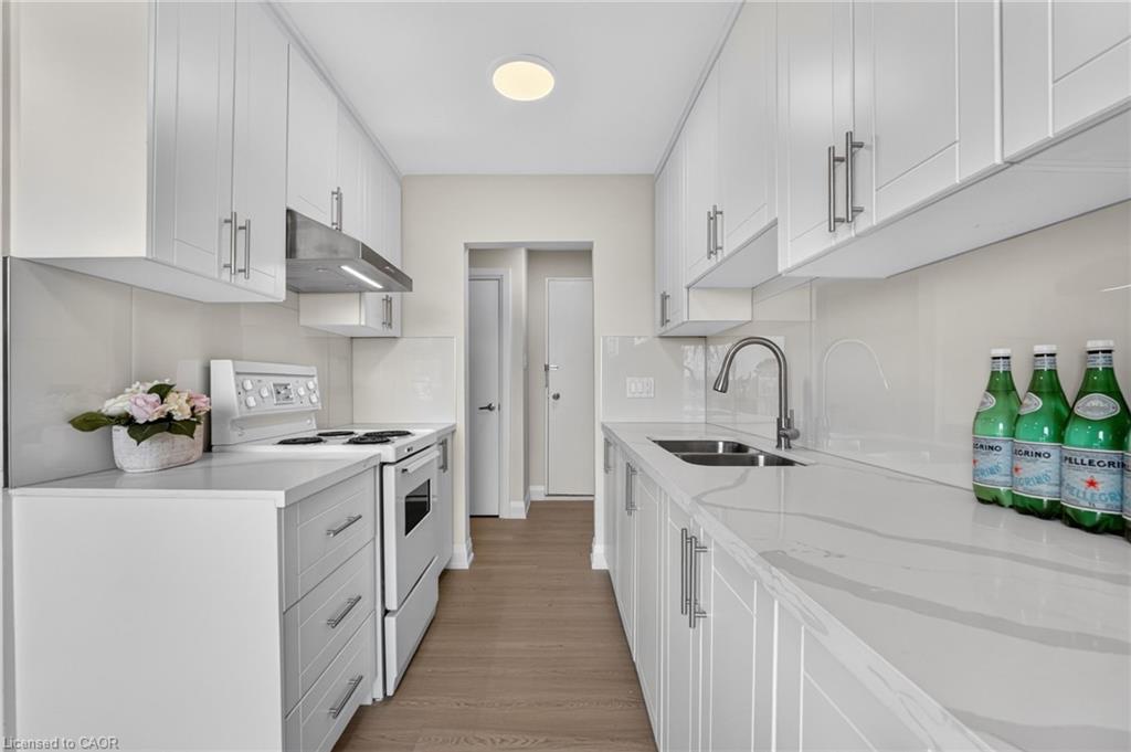 Galley kitchen with white cabinets, pale stone counters, stainless steel appliances, and wood-look flooring.