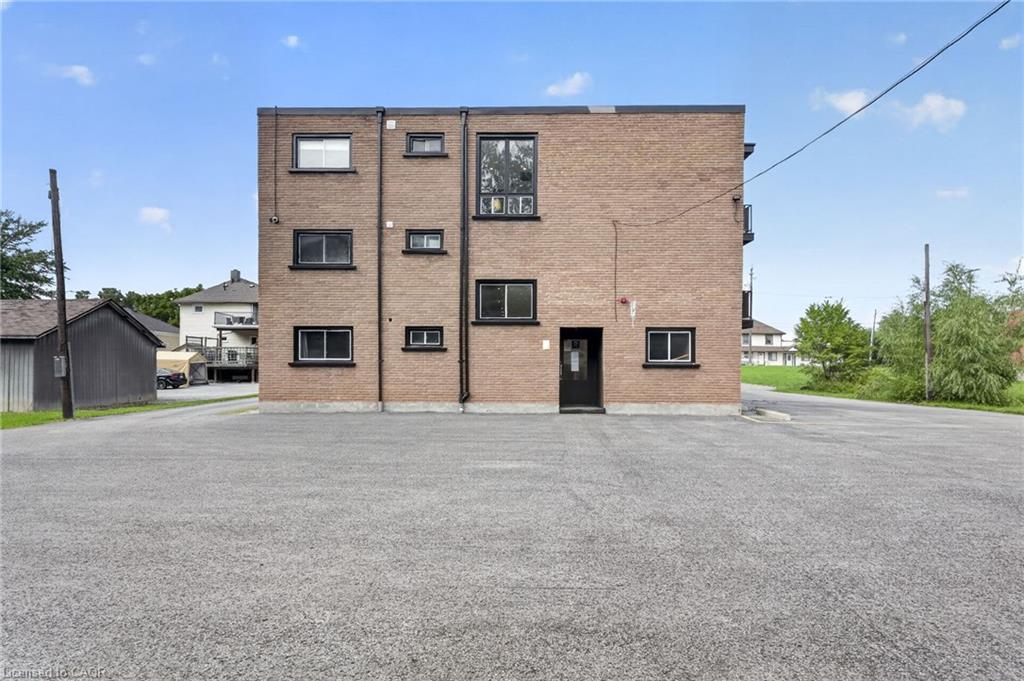 Three-storey brick apartment building with black-trimmed windows and a broad paved parking area.
