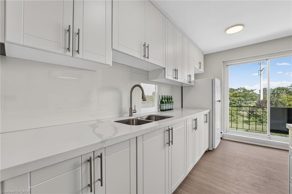 Modern white kitchen with a double-basin sink and sliding glass doors to a tree-lined balcony.