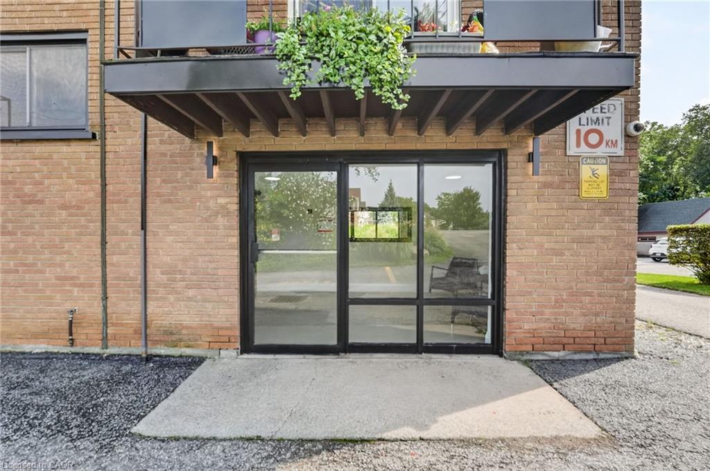 Brick condominium entrance with black-framed glass doors and a balcony with hanging greenery.