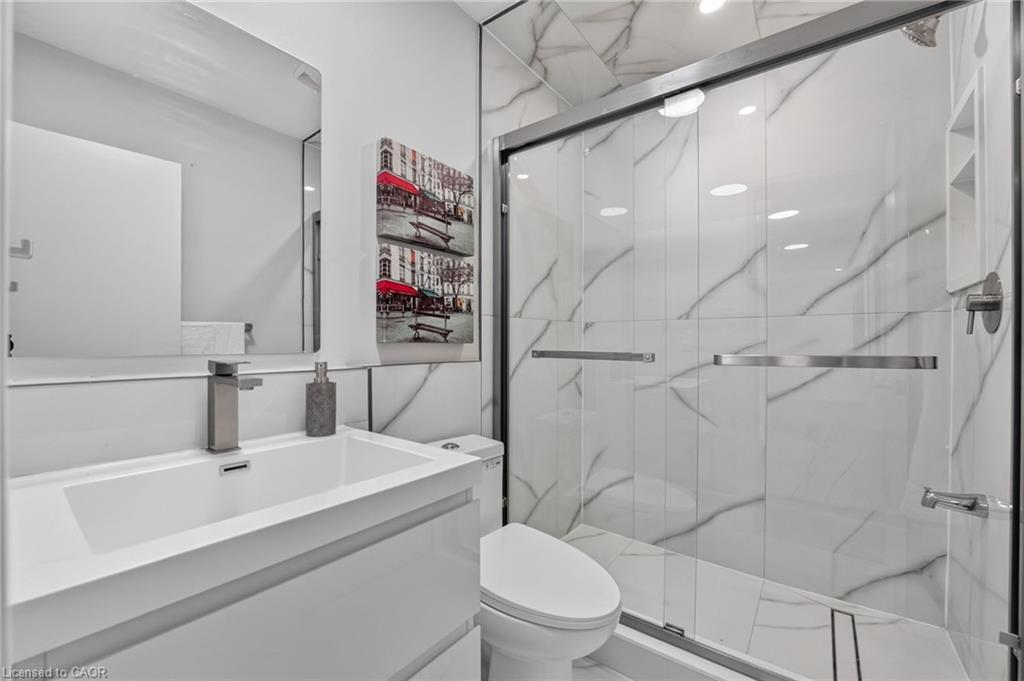 Modern bathroom with a glass-enclosed marble-look shower, white vanity, and toilet.