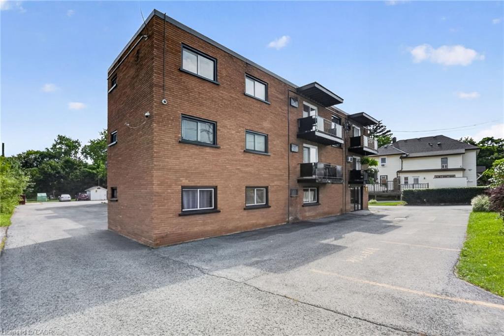 Three-story brown brick apartment building with balconies beside a paved parking area.