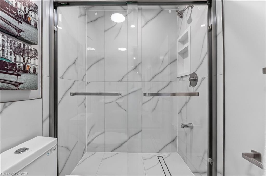 Glass-enclosed walk-in shower with marble-look tile, a recessed niche, and chrome fixtures.