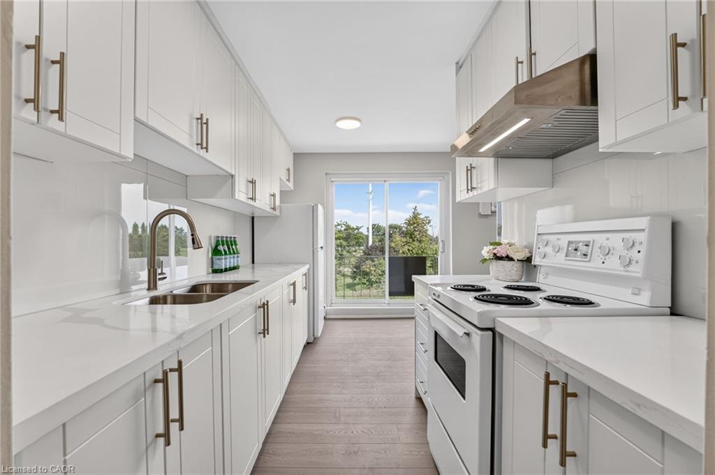 Bright white galley kitchen with double sink, electric range, and sliding doors to a balcony.