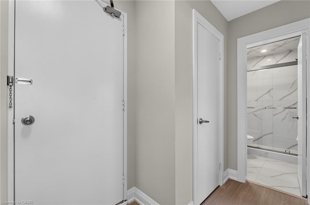 Hallway with a large white entry door and an open view into a tiled bathroom with glass shower.