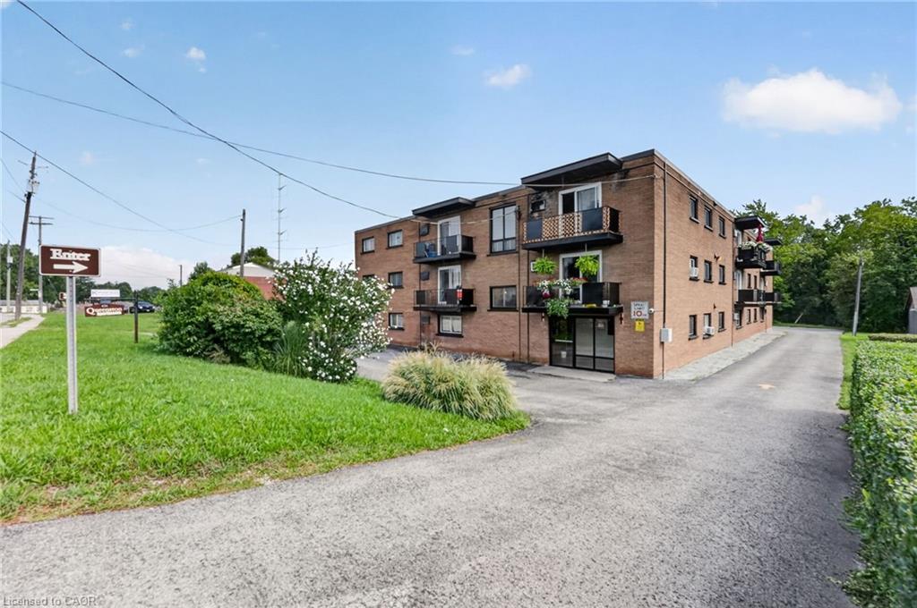 Three-storey brick apartment building with balconies beside a paved driveway and landscaped lawn.