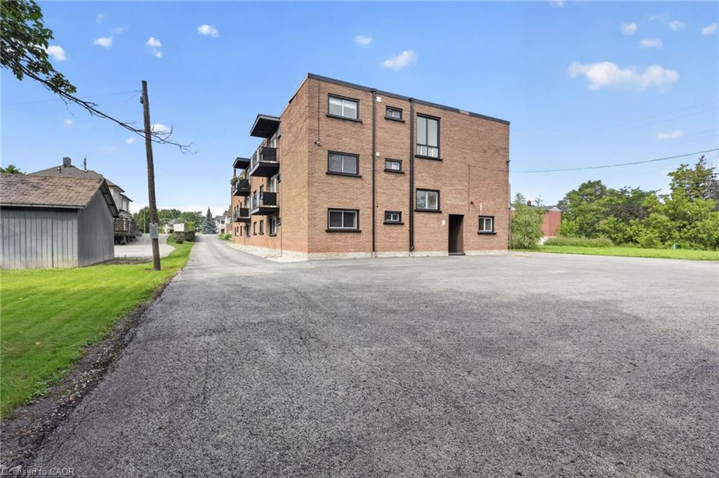 Brick apartment building with balconies beside a broad paved parking area.