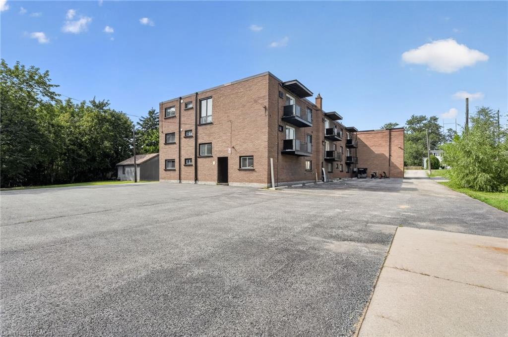 Brick apartment building with balconies beside a broad paved parking area.