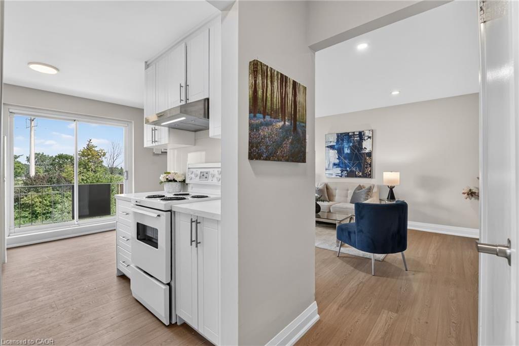 Open-plan condo kitchen and living room with white cabinets, a blue chair, and balcony doors.