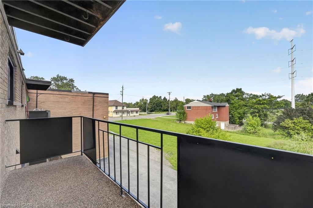 Apartment balcony overlooking a grassy area and nearby brick buildings.