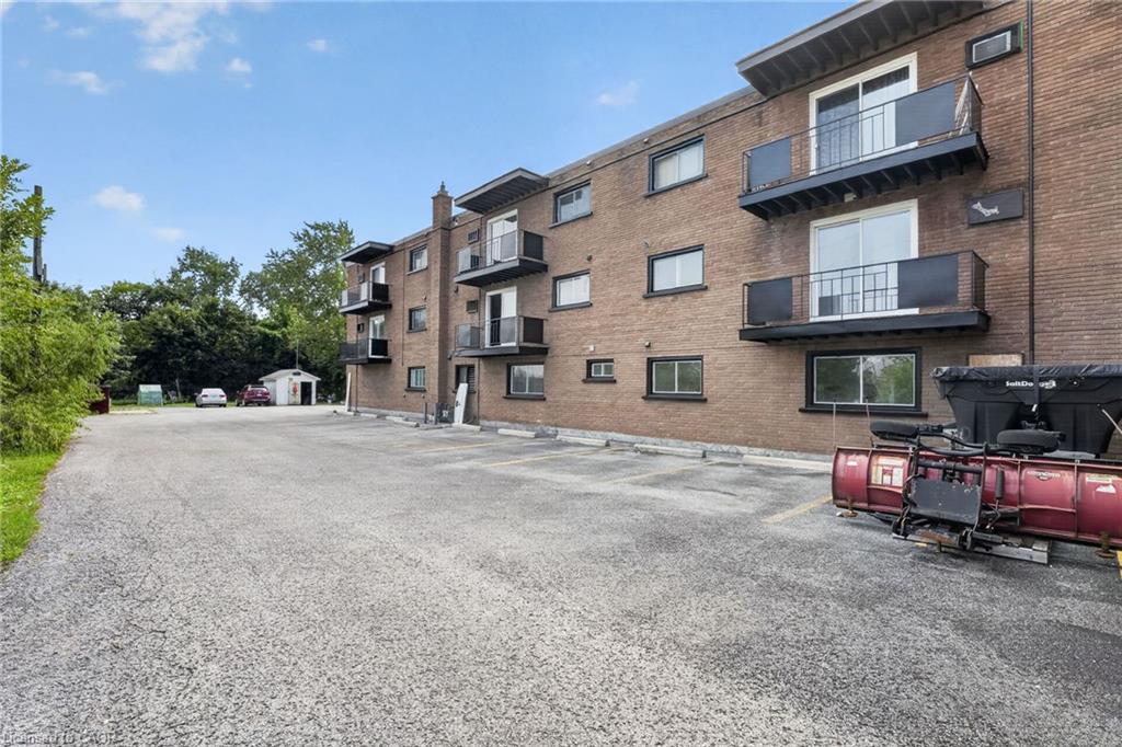 Brick apartment building with balconies beside a paved parking lot.