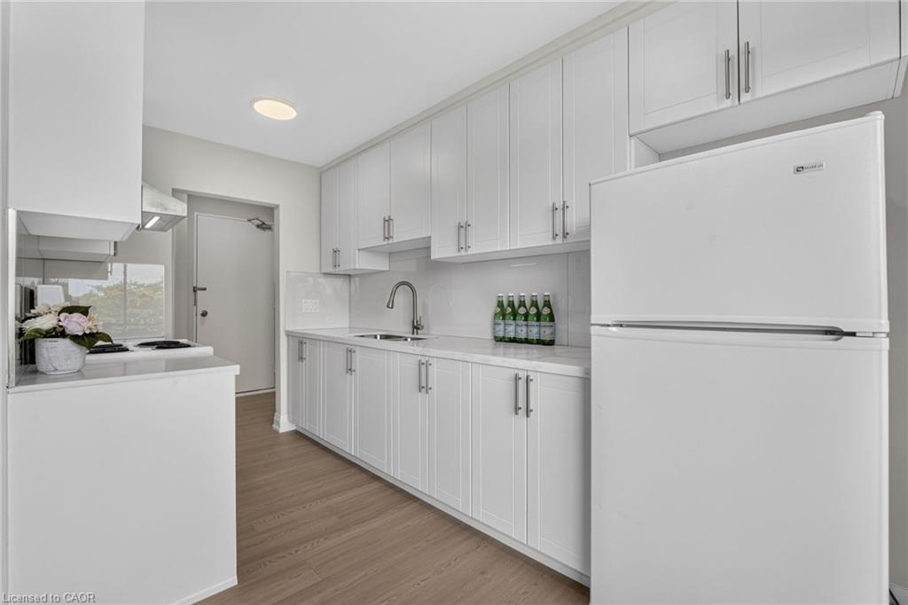 White kitchen with full-height cabinetry, a large refrigerator, and wood-look flooring.