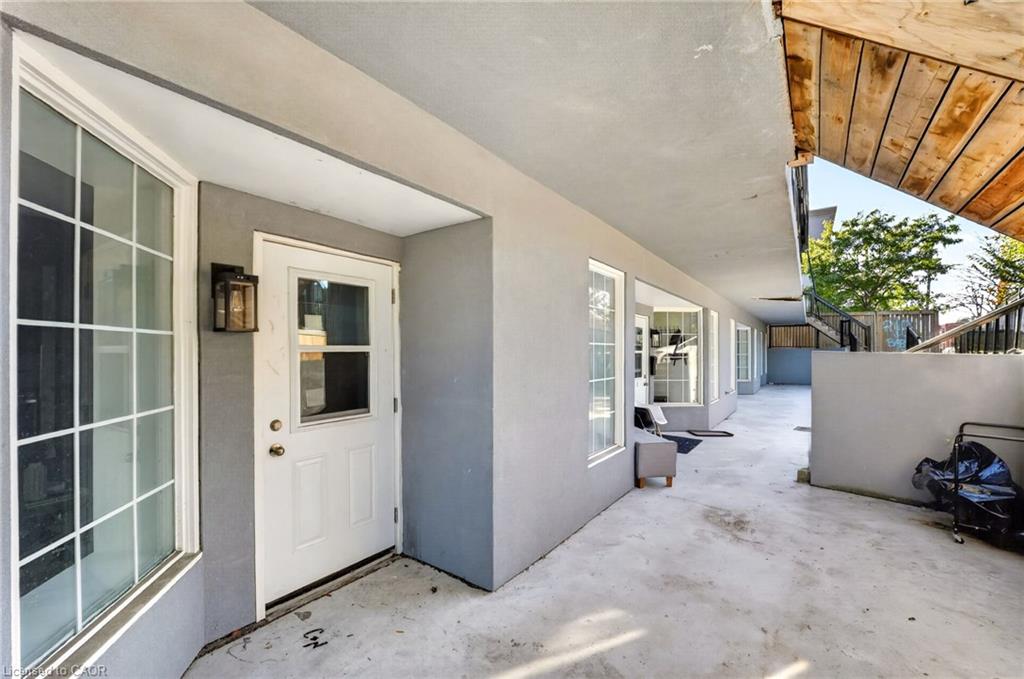 Covered concrete patio walkway beside a multi-unit building, with white doors and a wooden overhang.