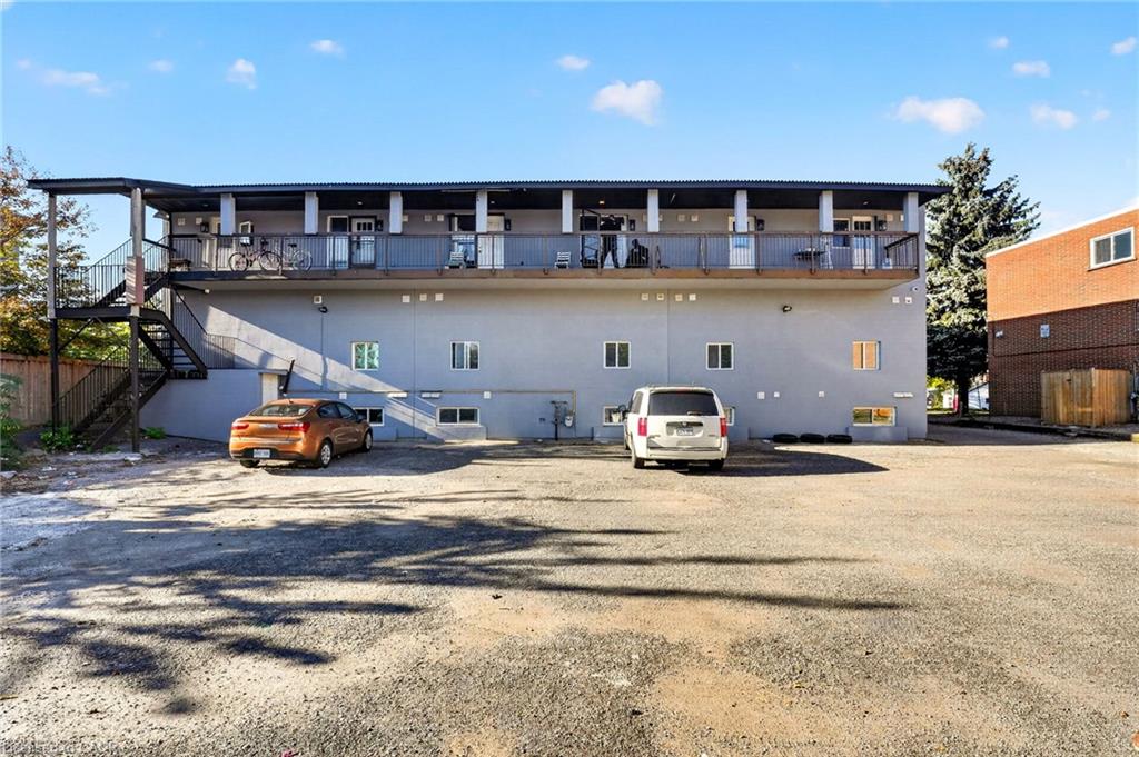 Residential building with an elevated balcony walkway and exterior stairs above a gravel parking area.