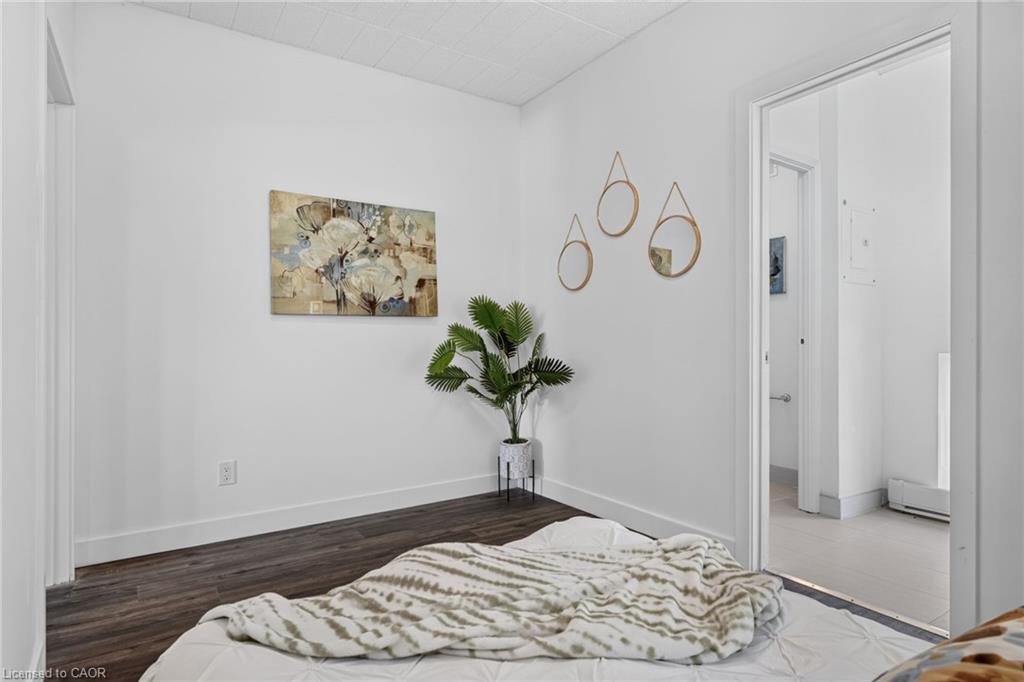 Staged bedroom with patterned bedding, dark flooring, wall art, and a potted plant.