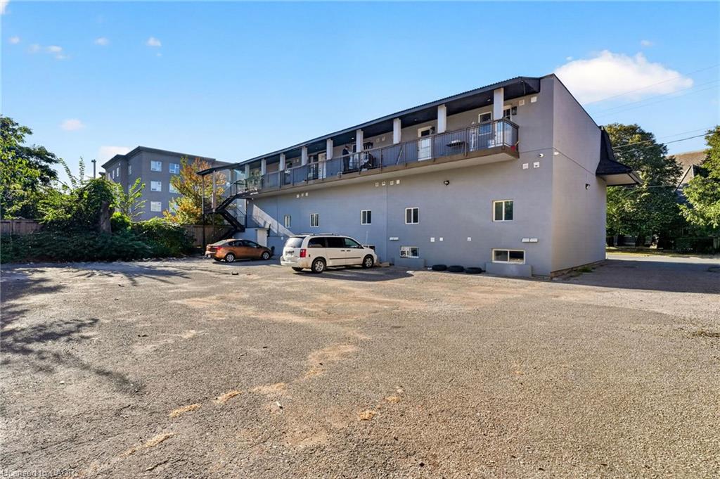 Rear exterior of a two-story apartment building with balconies, exterior stairs, and a parking lot.