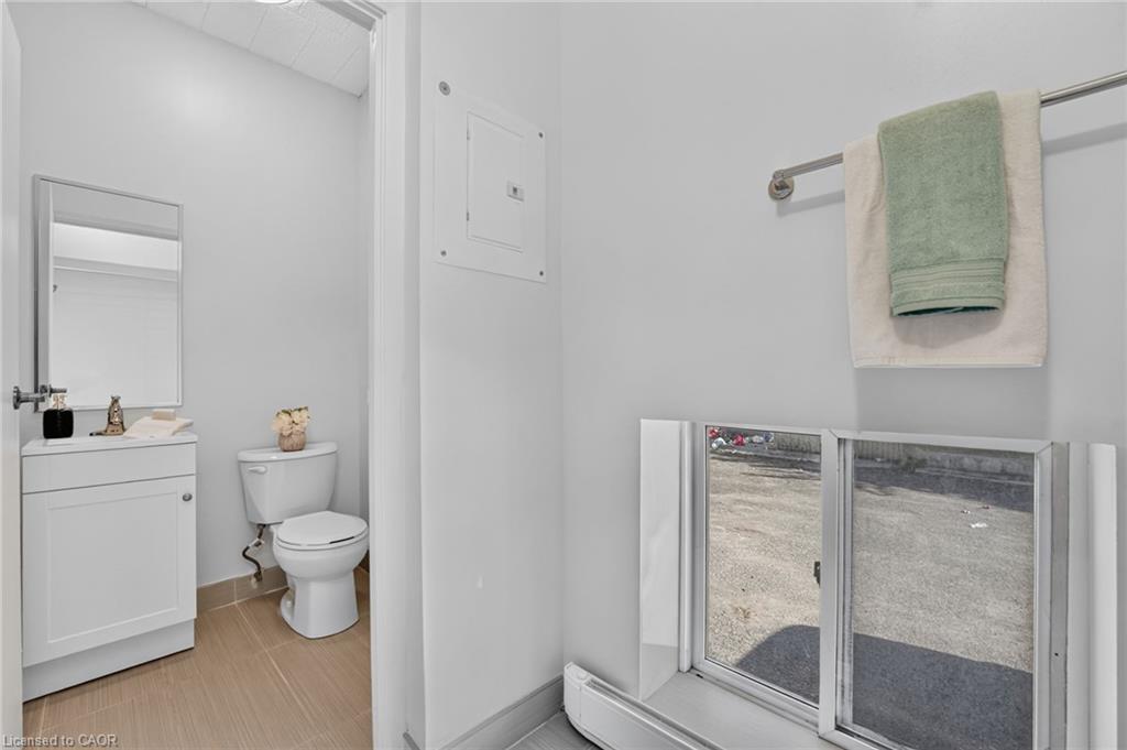 Bathroom with white vanity, toilet, and low sliding window beside hanging towels.