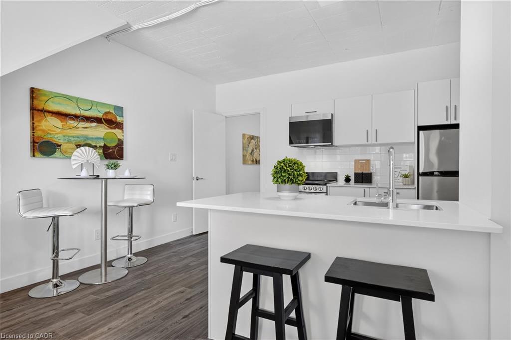 Modern white kitchen with a large island, stainless steel appliances, and dark wood-look flooring.