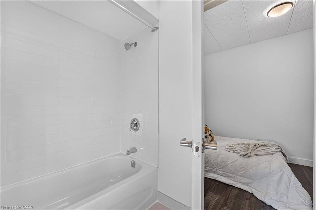 White-tiled bathroom with bathtub and shower, viewed through an open doorway beside a bedroom.