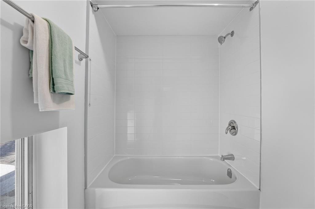 Bathroom bathtub with white tiled shower surround, glass screen, chrome fixtures, and towels.