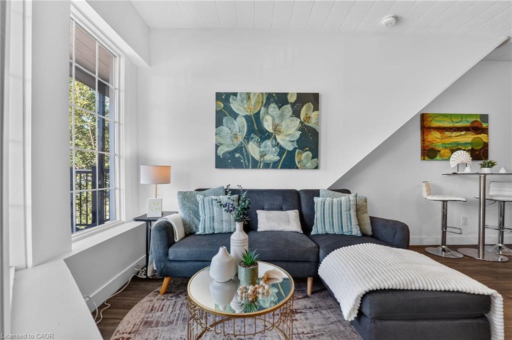Living room with a dark blue sofa, round glass coffee table, and large ottoman beside a tall window.
