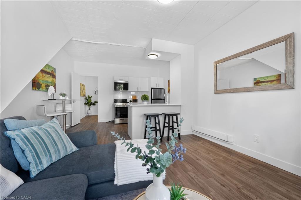 Open-plan condo living room with a blue sectional, white kitchen, breakfast counter, and wood-look flooring.