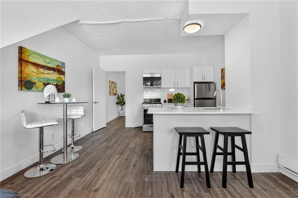 Open-plan kitchen with white cabinets, stainless appliances, and a peninsula with two black stools.