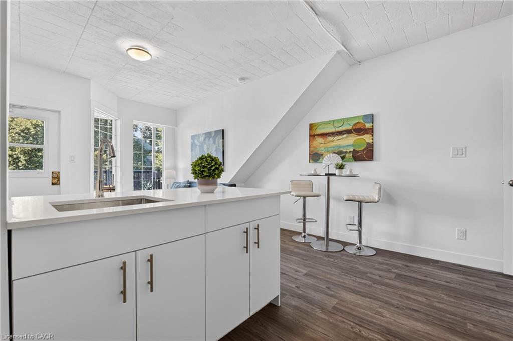 Kitchen with a large white island, tall windows, and two stools at a counter beneath a sloped ceiling.