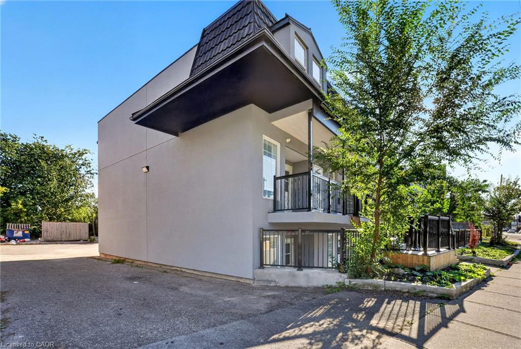 Modern multi-unit building with black balconies and landscaped sidewalk frontage.