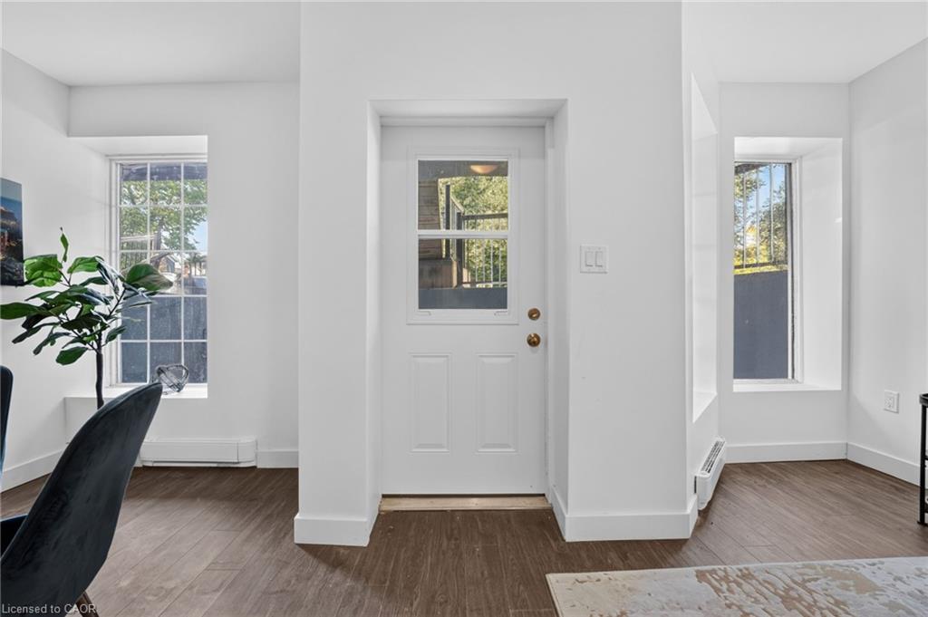 Bright entryway with a white glass-paneled front door, windows on either side, and wood-look flooring.