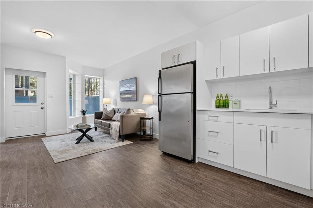 Open-plan kitchen and living area with white cabinetry, stainless refrigerator, and gray sofa.