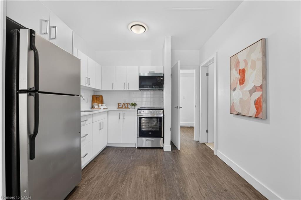 Kitchen with white cabinets, stainless steel appliances, and dark wood-look flooring.