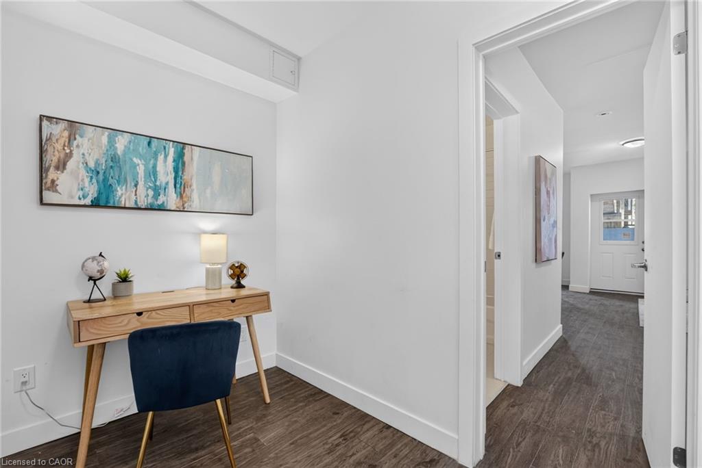 Furnished office nook with a wood desk and navy chair beside an open hallway.