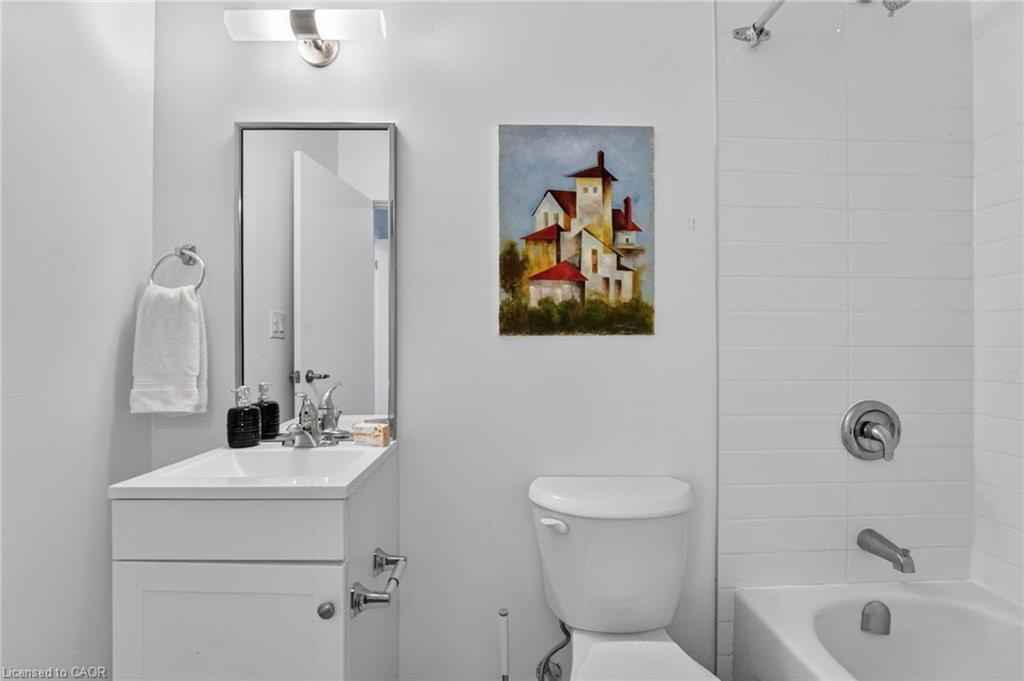 Bathroom with a white vanity, toilet, and tiled bathtub beside a colorful house painting.